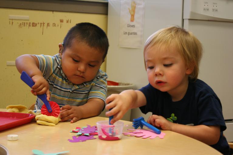 2 boys using tools to explore playdough while sitting at a table.
