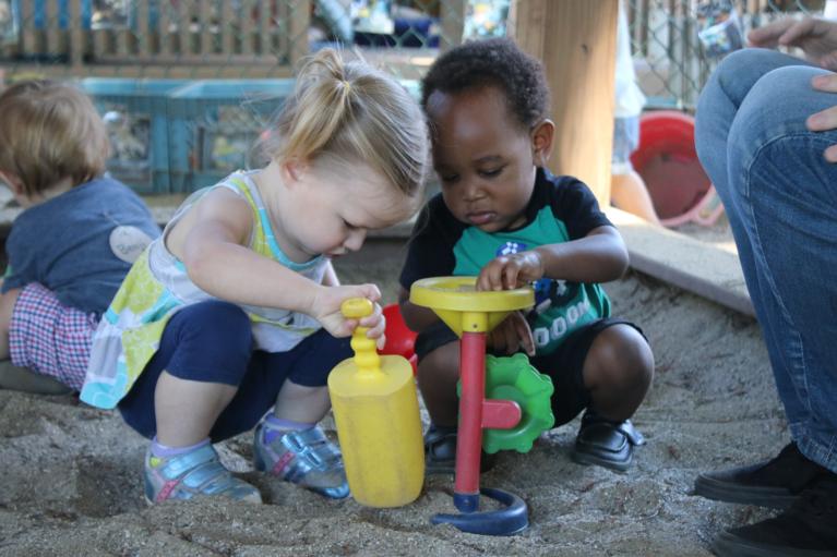 Two infants playing in the sandbox with sand toys